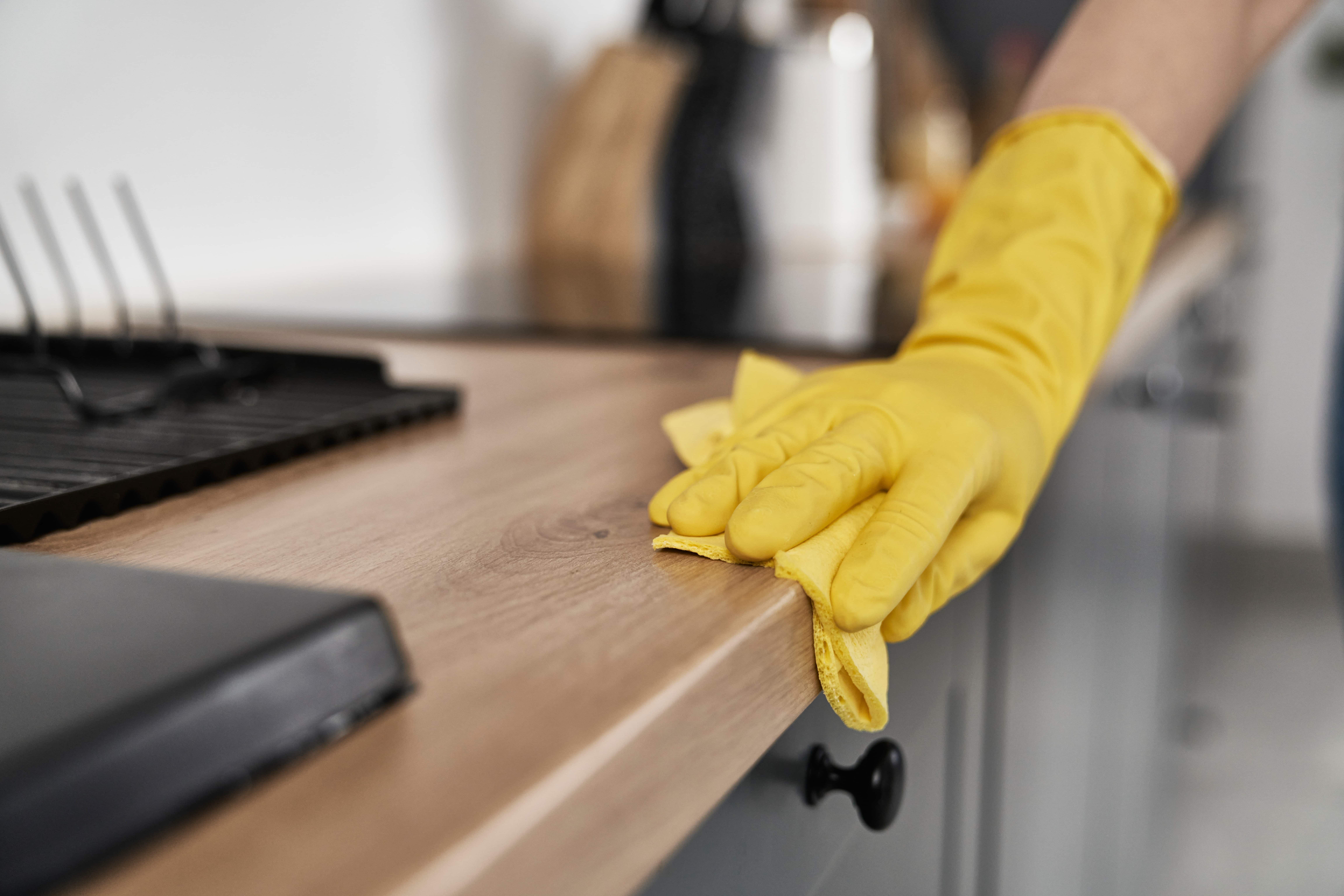 A gloved hand wiping down a timber kitchen benchtop
